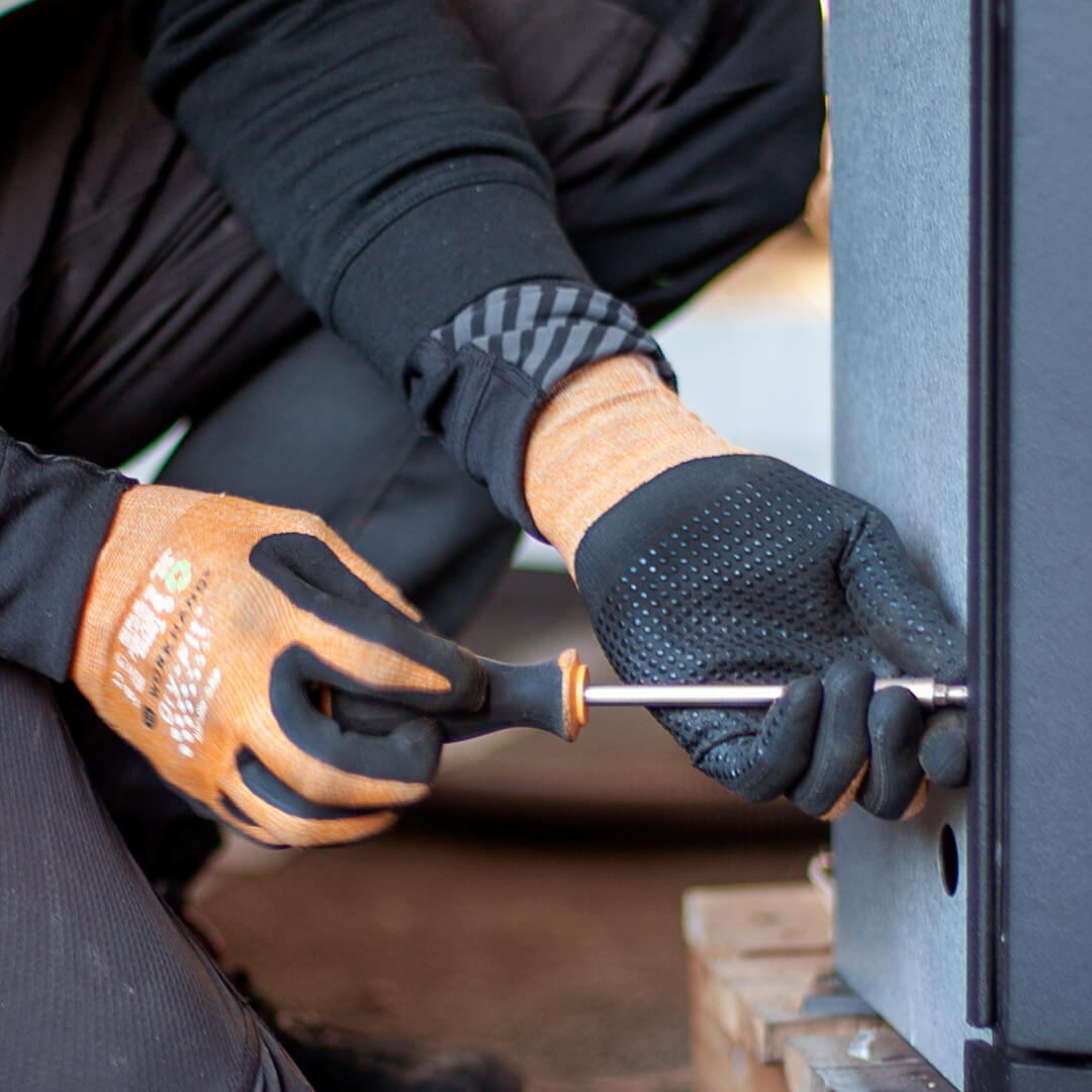 Fitter screwing on a wood-burning stove with a screwdriver