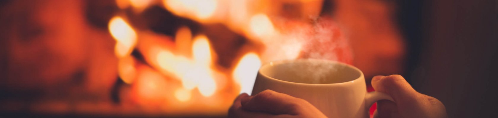 Female hands holding a white cup in front of an open fireplace with flames