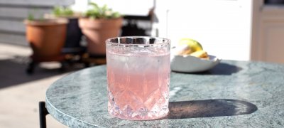Glass of rhubarb syrup summer drink on the porch with plants in the back