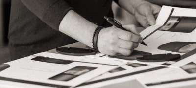 Black and white picture of a man's hands standing at a table and drawing on sketches of a Scan 87 wood stove
