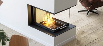 Picture taken from above of large fireplace insert Scan 5005 FRL with glass on three sides and sliding door on rustic wooden floor and brown leather chair next to it