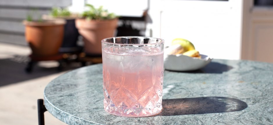 Glass of rhubarb syrup summer drink on the porch with plants in the back