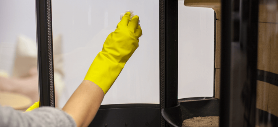 Hand with yellow rubber glove that washes soot off the fireplace glass on an oven