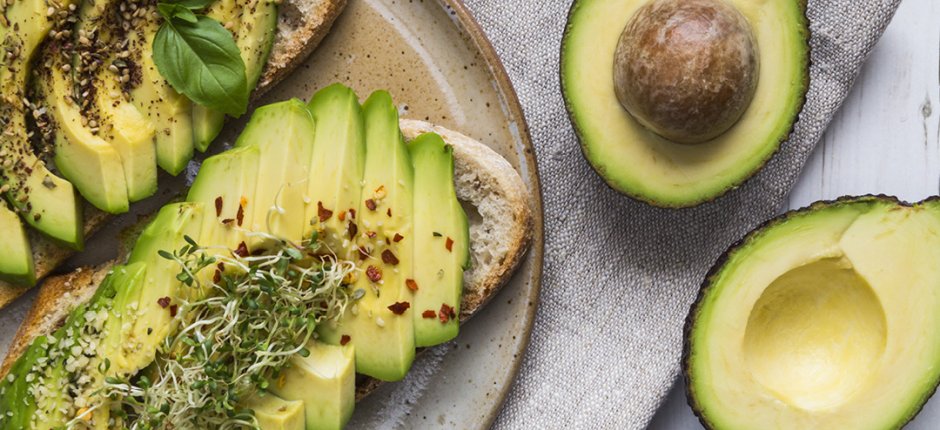 Plate with two avocado toast on a white table and two halves of avocado laying on a linen napkin