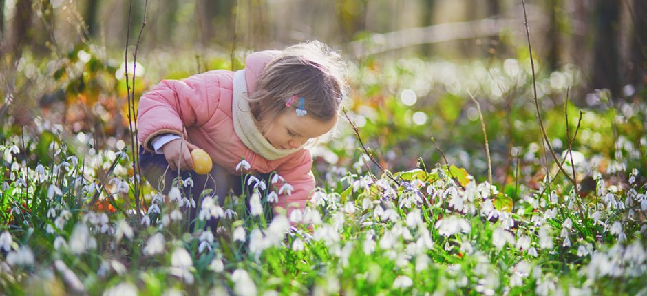 Little girl with jacket looking for Easter eggs in nature