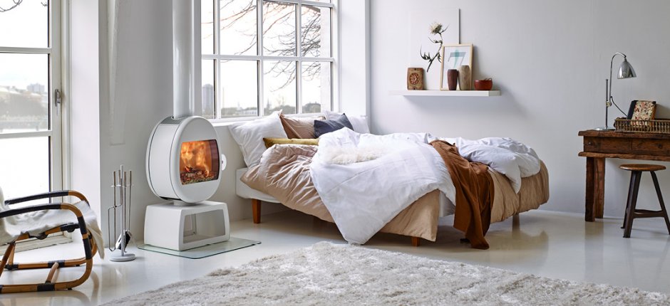 White stove Scan 66 in a white room cabin next to a bed and a wooden desk