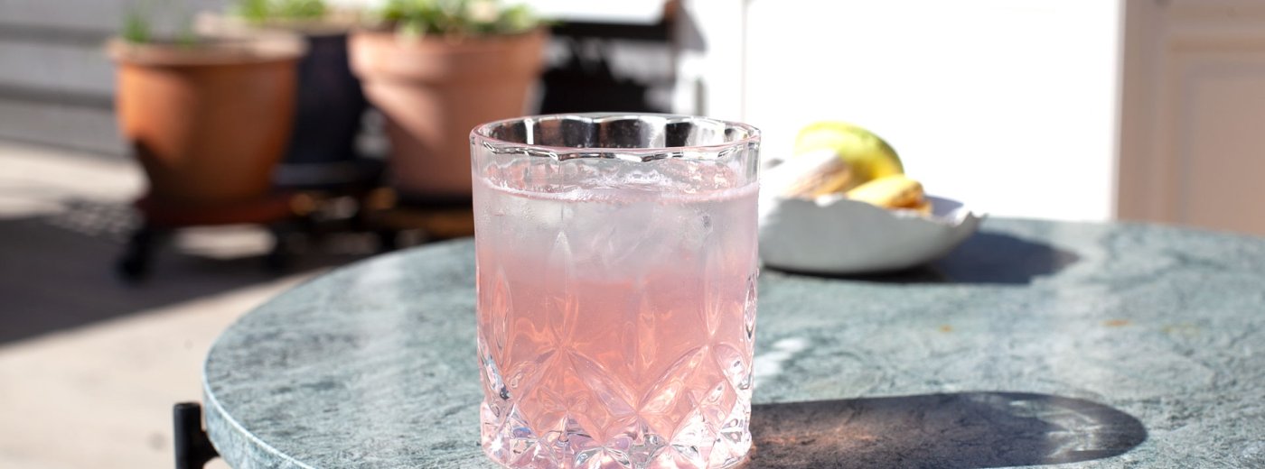 Glass of rhubarb syrup summer drink on the porch with plants in the back