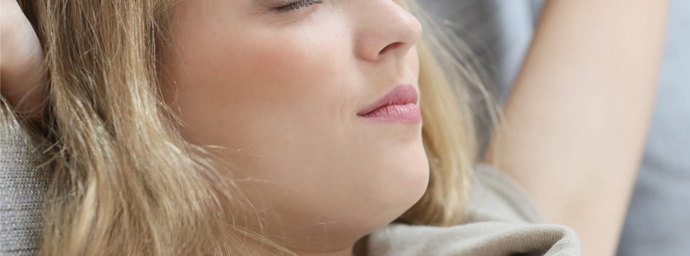 Blonde woman with closed eyes resting on sofa