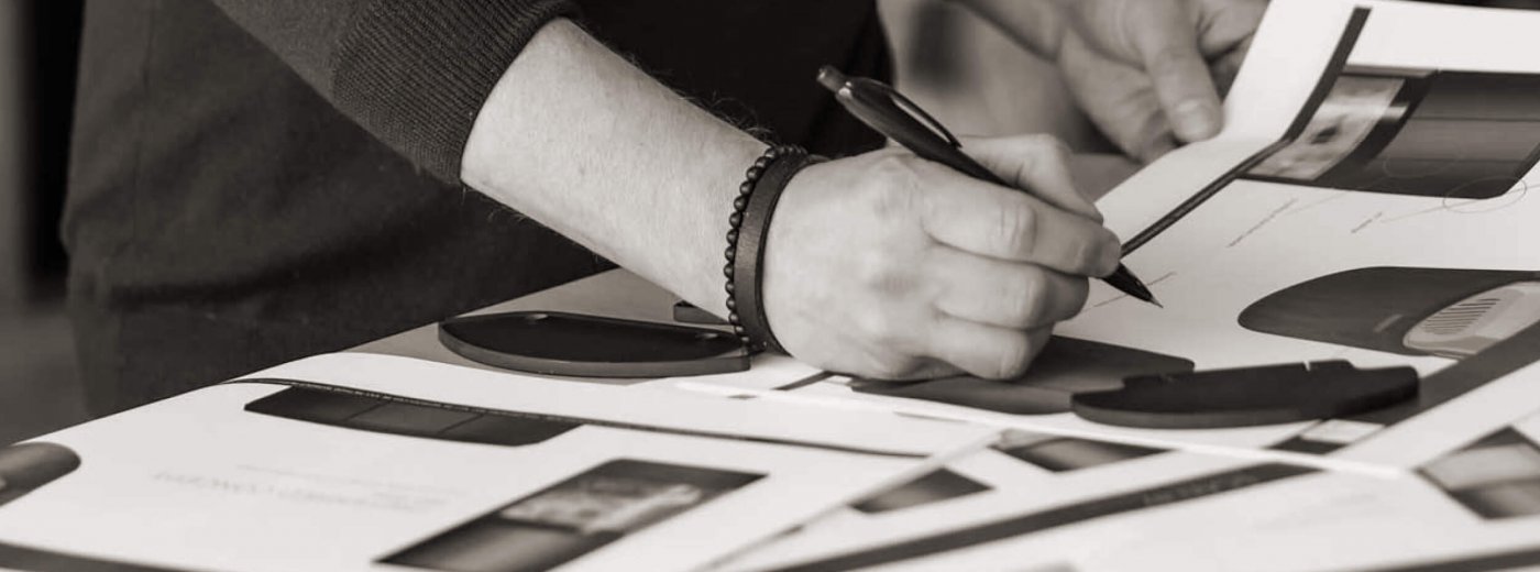Black and white picture of a man's hands standing at a table and drawing on sketches of a Scan 87 wood stove
