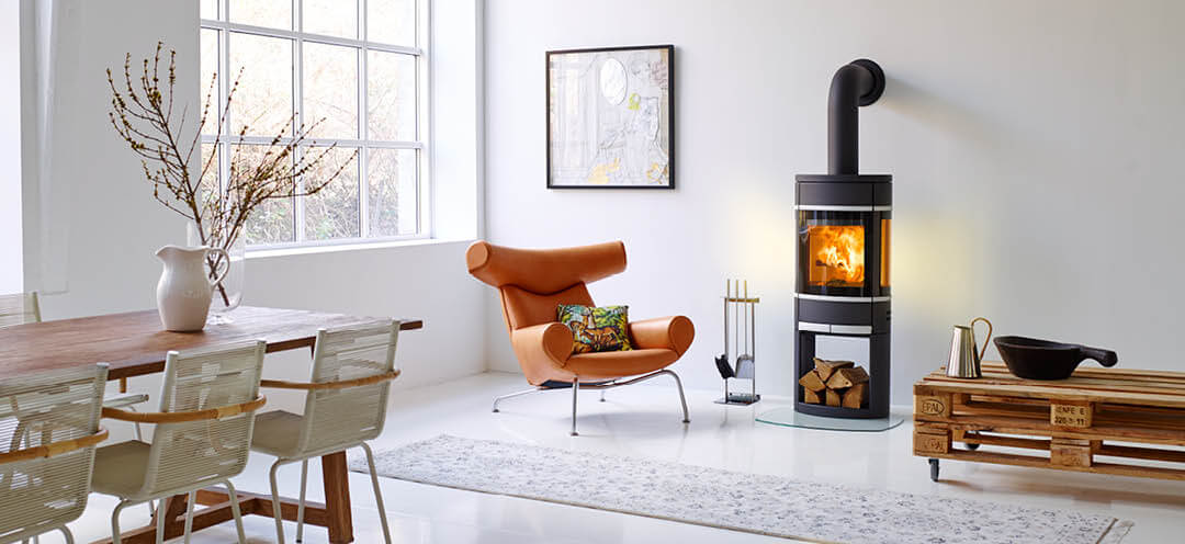 Black oval Scan 68 wood stove in a white room with a designer chair in bright leather and a rough pallet table with wheels