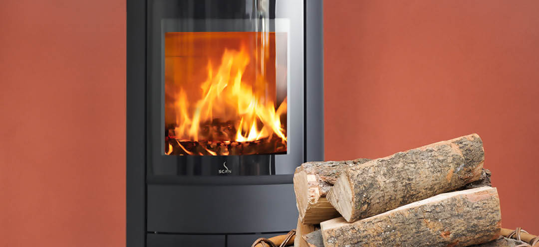 Black oval wood-burning stove Scan 68-13 in red room with a large basket of wood in front