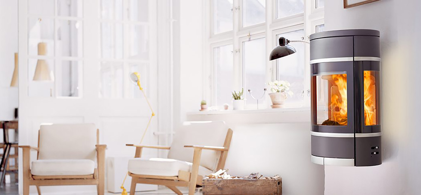 Black oval wall-hung wood burning stove with side glass aluminum handle and decorative strips Scan 68-8 in a white room with light furniture in Danish design style