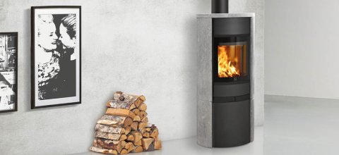 Black wood-burning stove with soapstone sides Scan 68-15 in white room with a stack of wood placed next to it